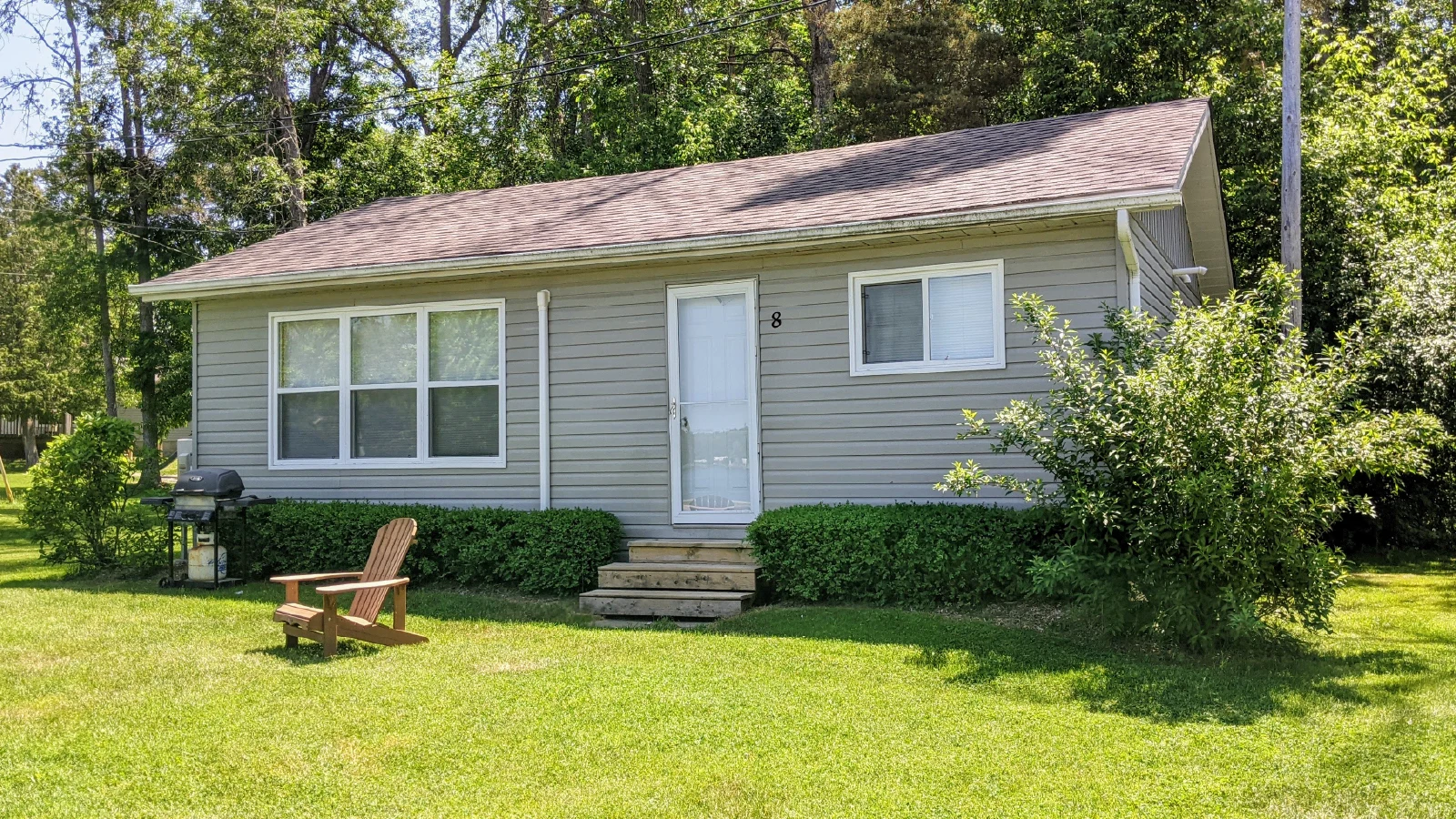 Pigeon Lake Resort Cottage 8 exterior with front steps, large windows, lawn, barbecue, and outdoor chair.